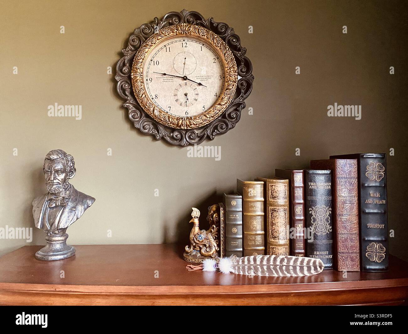 Vintage-Buchsammlung mit einem antiken, pfauenförmigen Buchende, einer antiken Uhr, einer Lincoln-Statue und einer Adlerfeder. Stockfoto