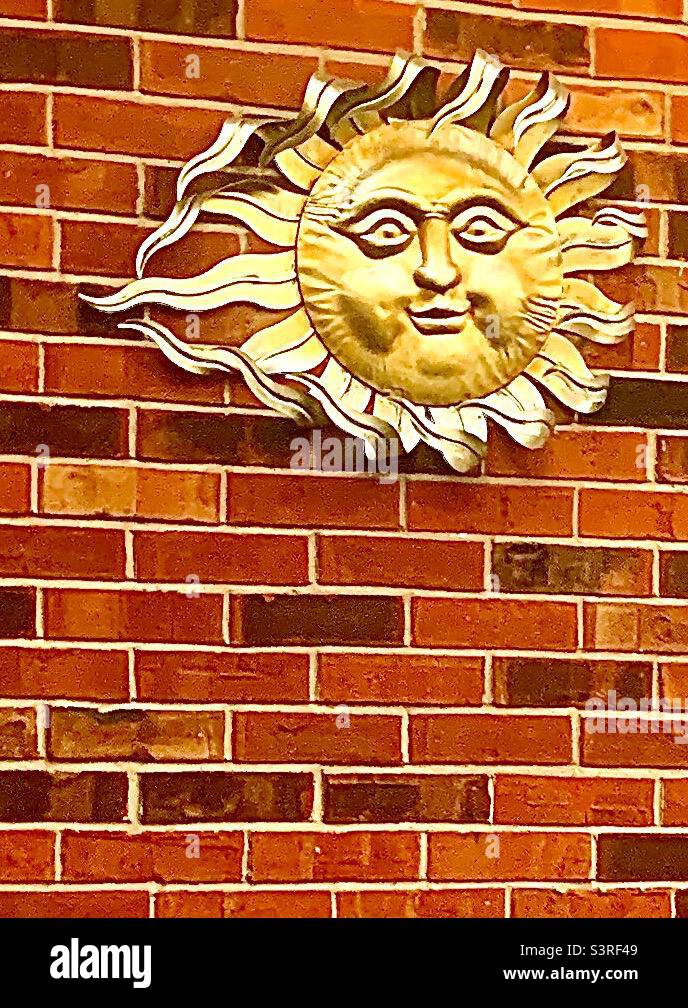 Lächelndes goldenes Sonnenzubehör in der oberen Ecke der roten Ziegelwand Stockfoto
