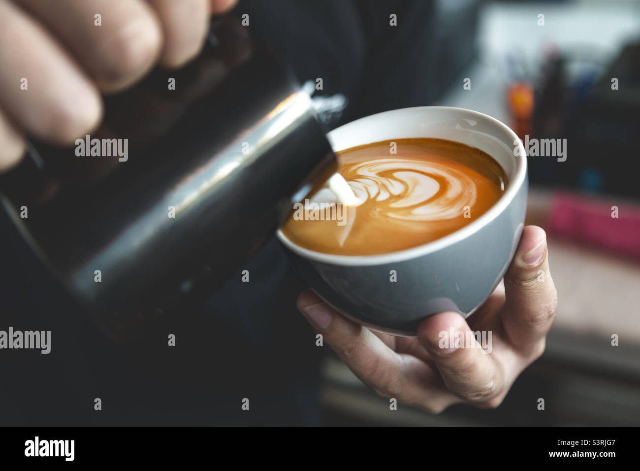 Barista bereitet Café Latte zu, gießt Milch in eine Tasse Kaffee. Nahaufnahme von Latte Art. Stockfoto