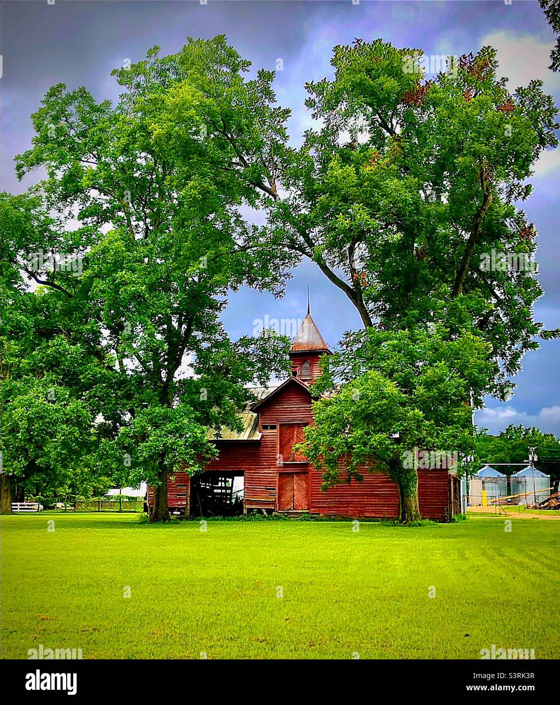 Rote Scheune zwischen zwei Bäumen unter bewölktem Himmel im ländlichen South Carolina, USA. Einfach Nur South Carolina Stockfoto