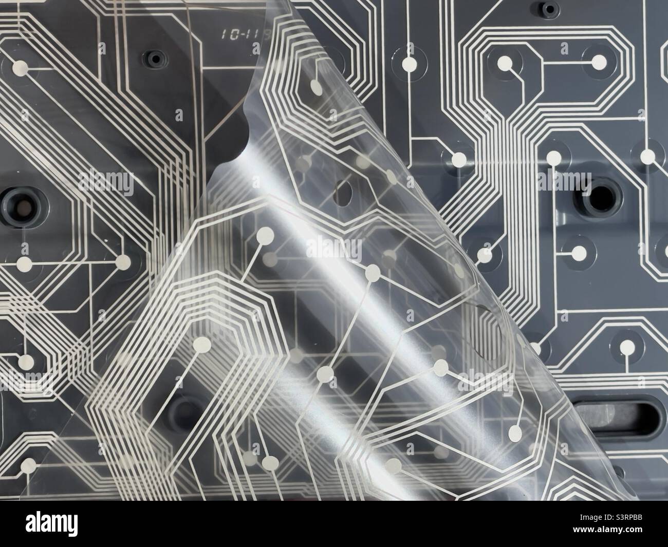 Zwei von einer alten Tastatur entnommenen Schichten der gedruckten Schaltung, die obere Schicht wurde nach hinten gebogen, um die darunter liegende zweite Schicht vor einem dunklen Hintergrund zu zeigen Stockfoto