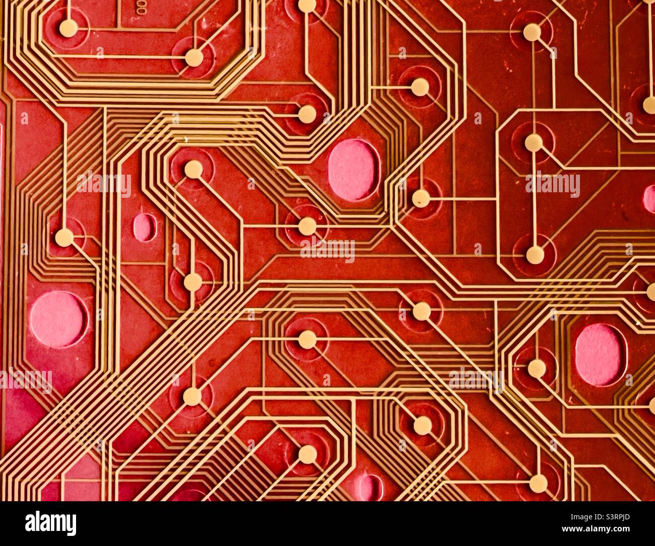 Ein Detail einer gedruckten Schaltung von einer alten Tastatur vor einem roten Hintergrund Stockfoto