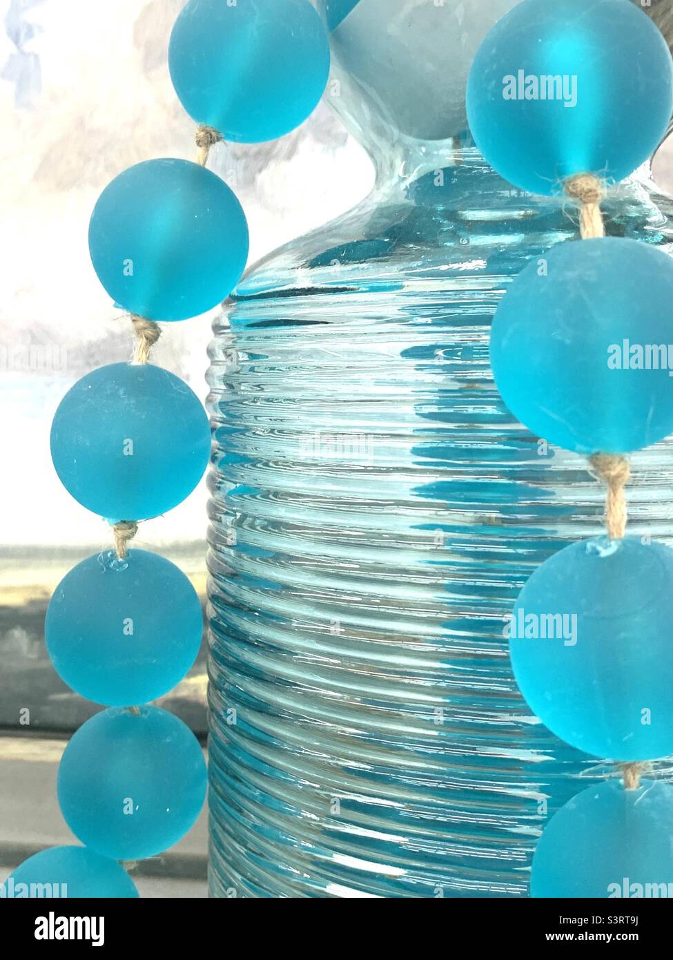 Schöne, helle Komposition aus großen aquafarbenen kugelförmigen Perlen und transparenter Vase Stockfoto