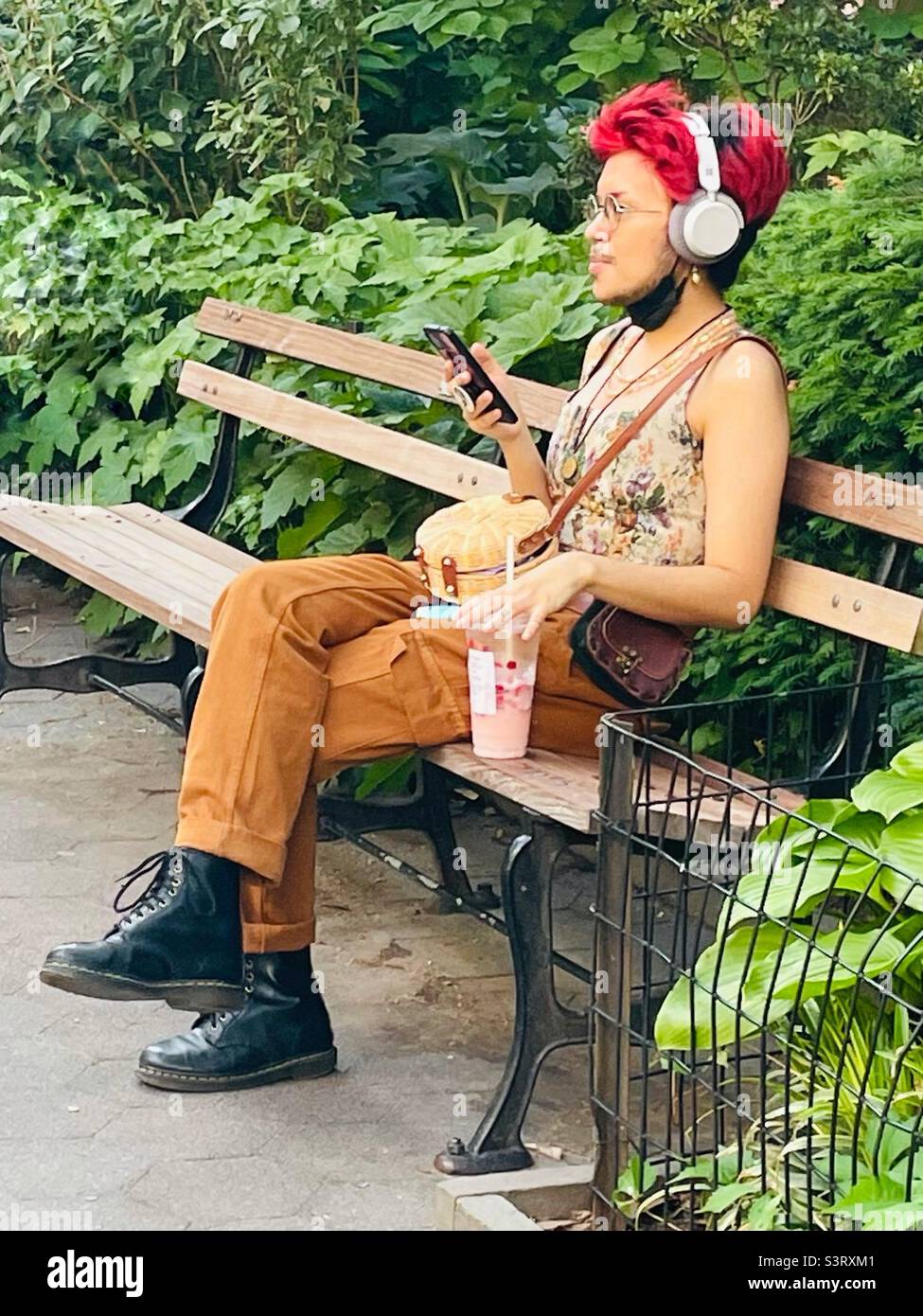 Person, die im Park sitzt und mit Kopfhörern zuhört - Smartphone-aufgenommenes Stockfoto