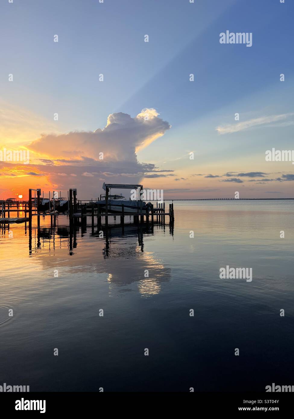 Dramatischer Sonnenuntergang Himmel mit Sonnenstrahl und Reflexionen über dem Bay Water Stockfoto