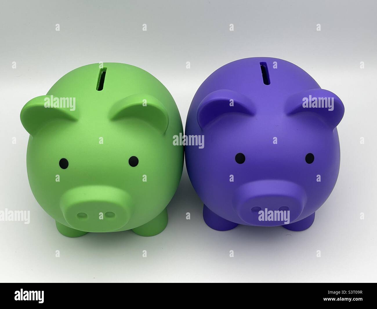 Zwei unterschiedlich gefärbte Sparschweinebänke für Kinder, violett und lindgrün, sitzen nebeneinander. - Smartphone-aufgenommenes Stockfoto