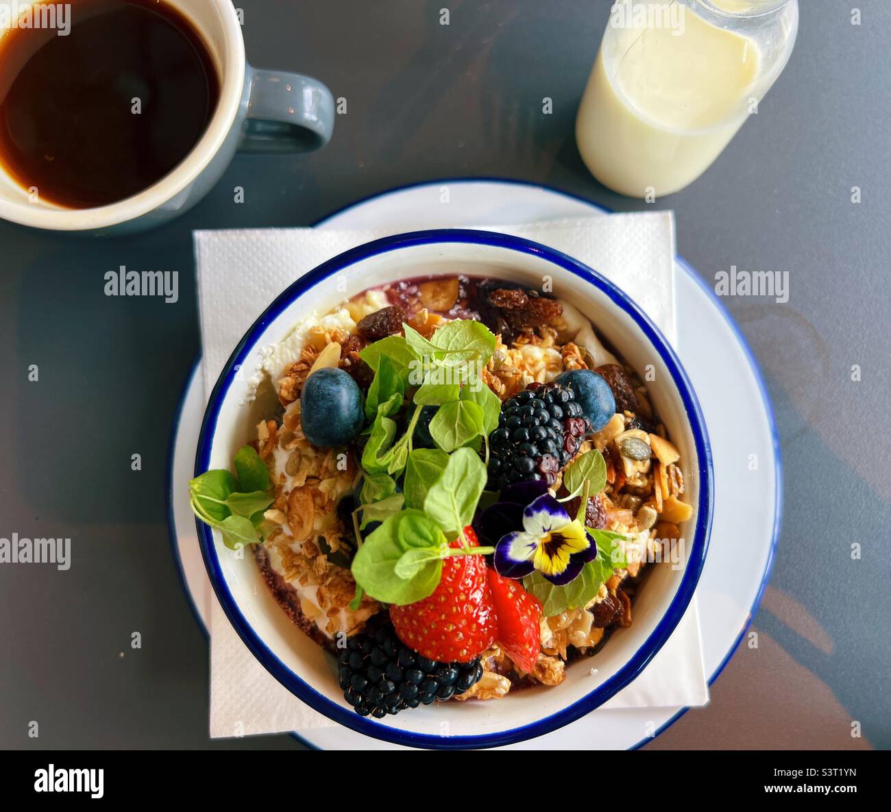 Müsli mit Obst und Minze und schwarzem Kaffee und Milch auf der Seite Stockfoto