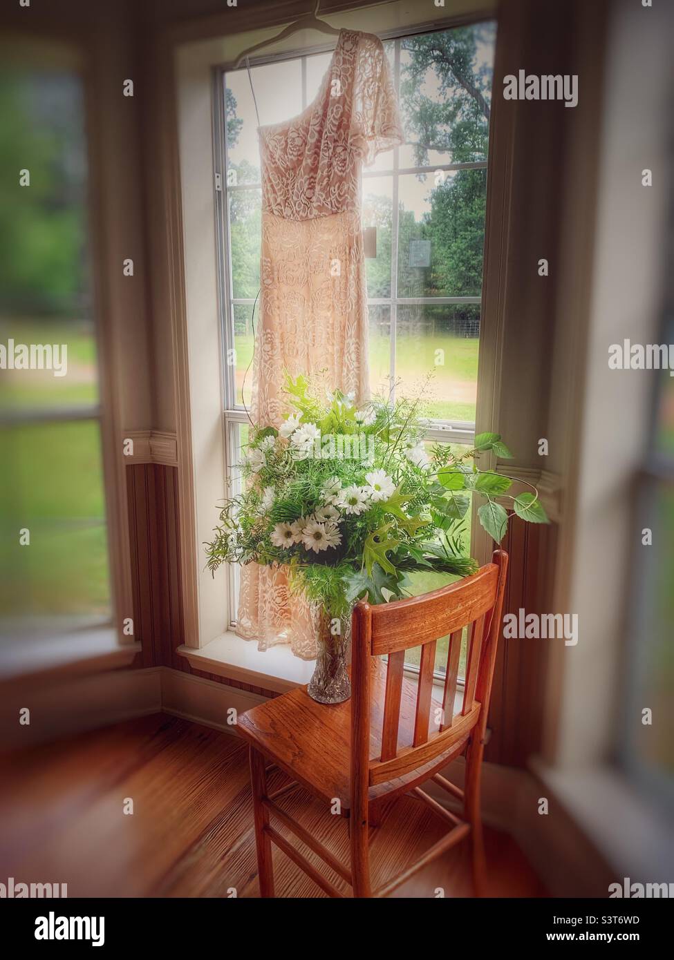 Vintage Stuhl mit Hochzeitsblumen und Hochzeitskleid im Fenster am heißen südlichen Sommertag Stockfoto