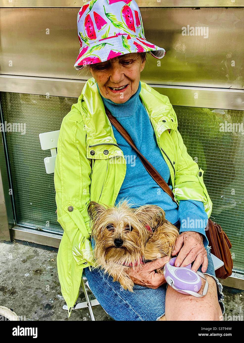 Eine Frau in farbenfrohem Regengeschirr mit einem entzückenden Yorky-Hund auf ihrem Schoß Stockfoto