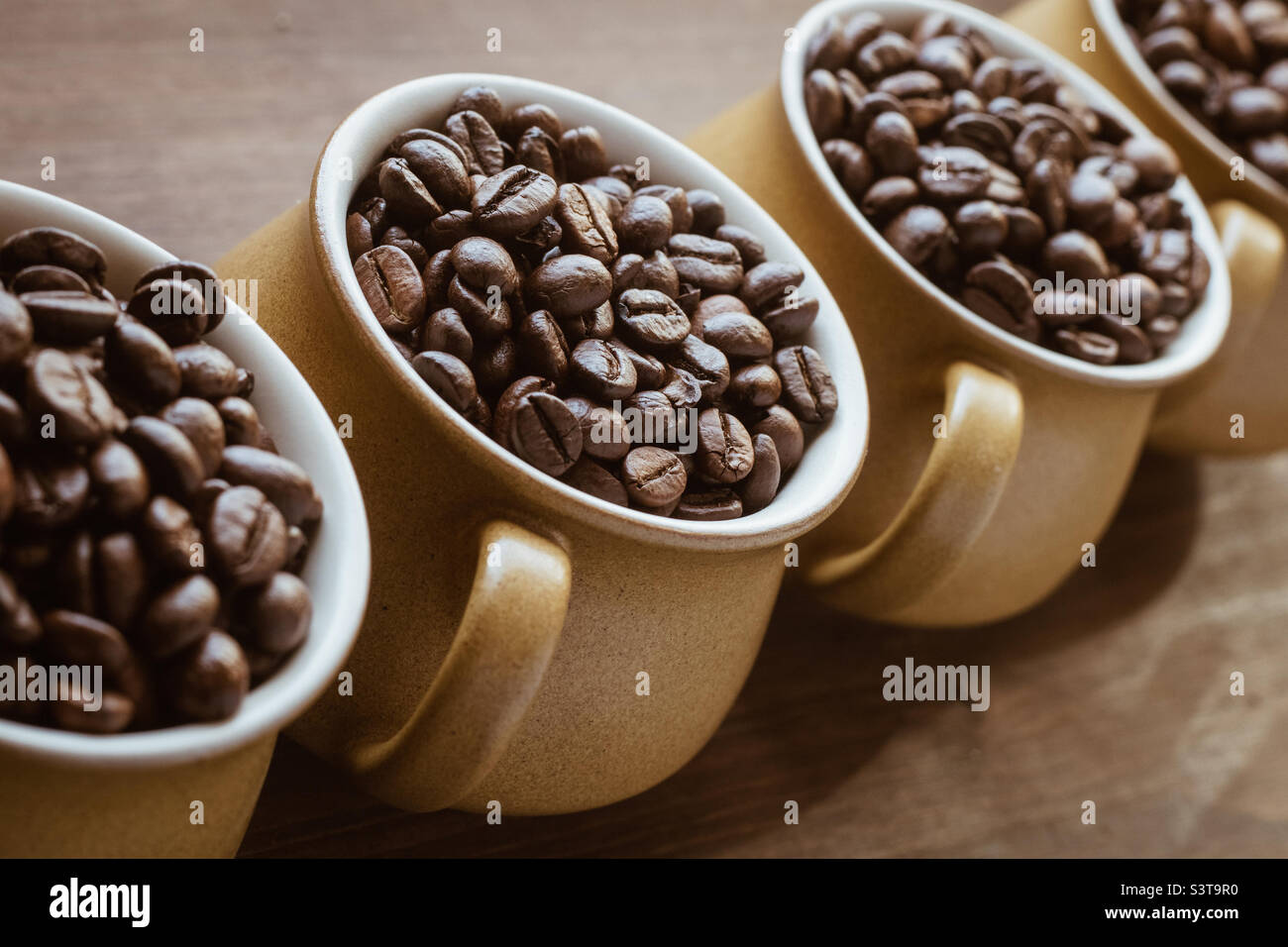 Eine Reihe von 4 Kaffeetassen, gefüllt mit Kaffeebohnen vor einem Holzhintergrund - Smartphone-aufgenommenes Stockfoto