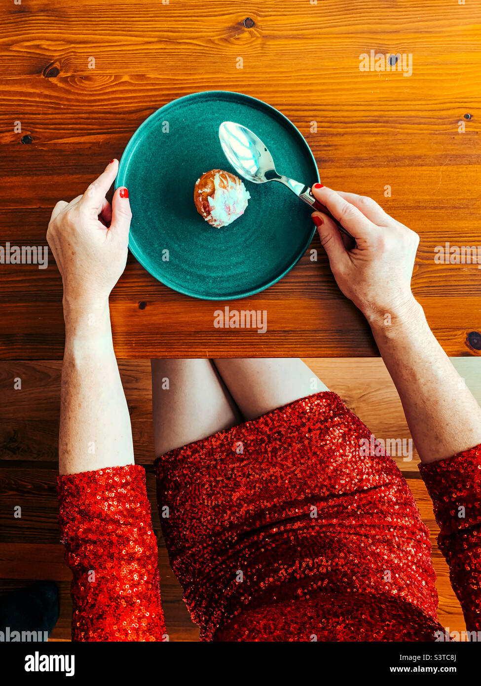 Draufsicht auf eine Frau, die ein rotes Paillettenkleid trägt und Profiterolen isst Stockfoto