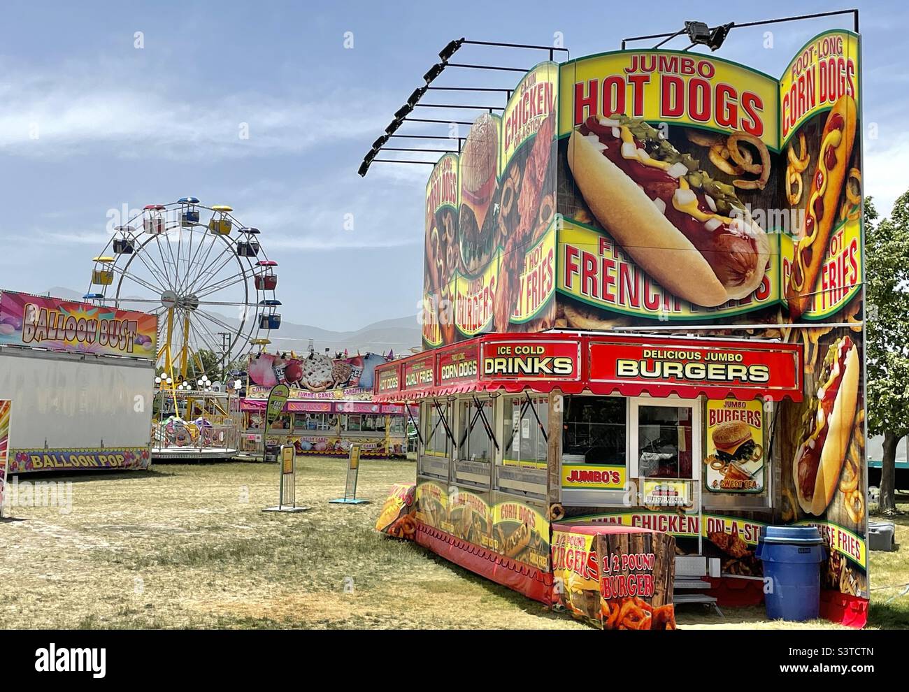 Ein Wanderkarneval, der für das jährliche West Fest in Utah, USA, eingerichtet wird. Im Hintergrund ist ein Riesenrad zu sehen und im Vordergrund ein Foodstand. Bald kommt die Eröffnung und die Massen. Stockfoto