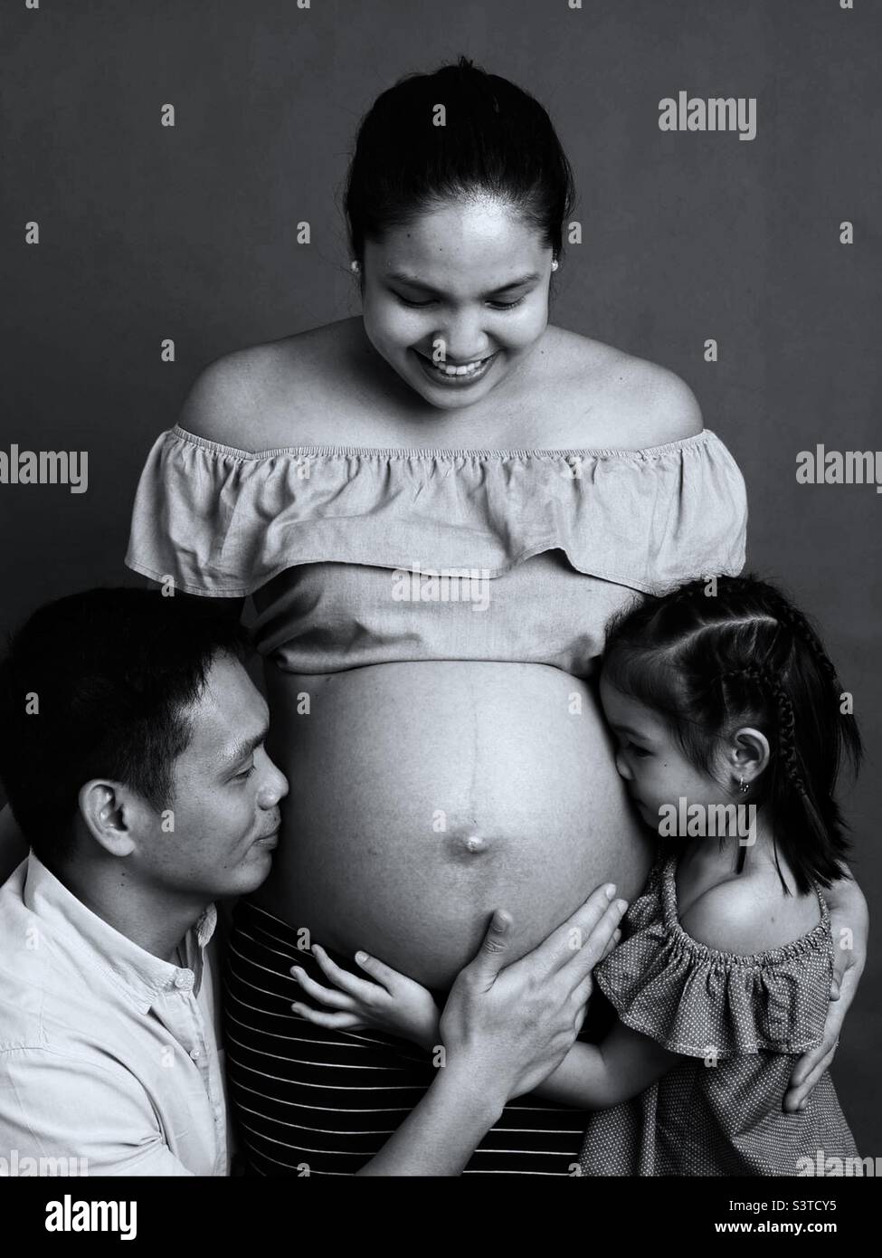Eine Schwangerschaftsmutter zeigt ihrer Tochter und ihrem Mann ihren Bauch. Stockfoto