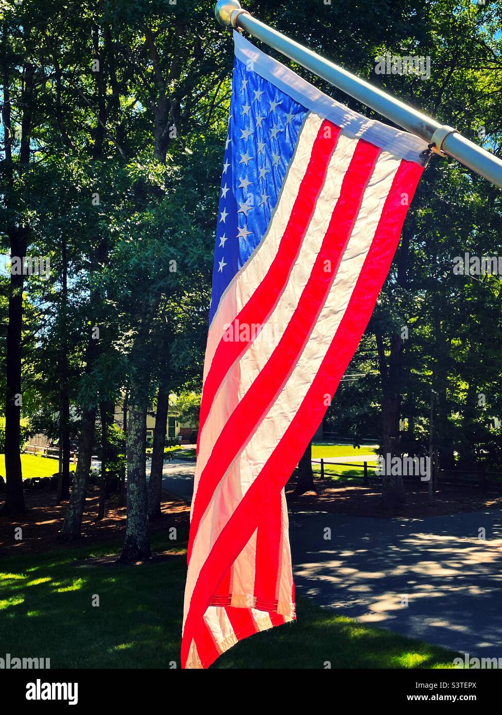 Eine amerikanische Flagge hängt anmutig auf einem gehobenen Vorstadthaus vor einem gepflegten Vorgarten, Summertime 2022, USA - Smartphone-aufgenommenes Stockfoto