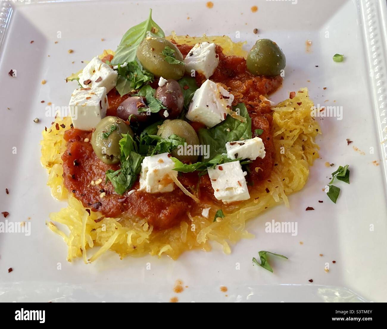 Spaghetti-Kürbis mit Tomatensauce, grünen Oliven, Basilikum, Feta-Käse und zerkleinerten roten Paprika-Samen. Stockfoto