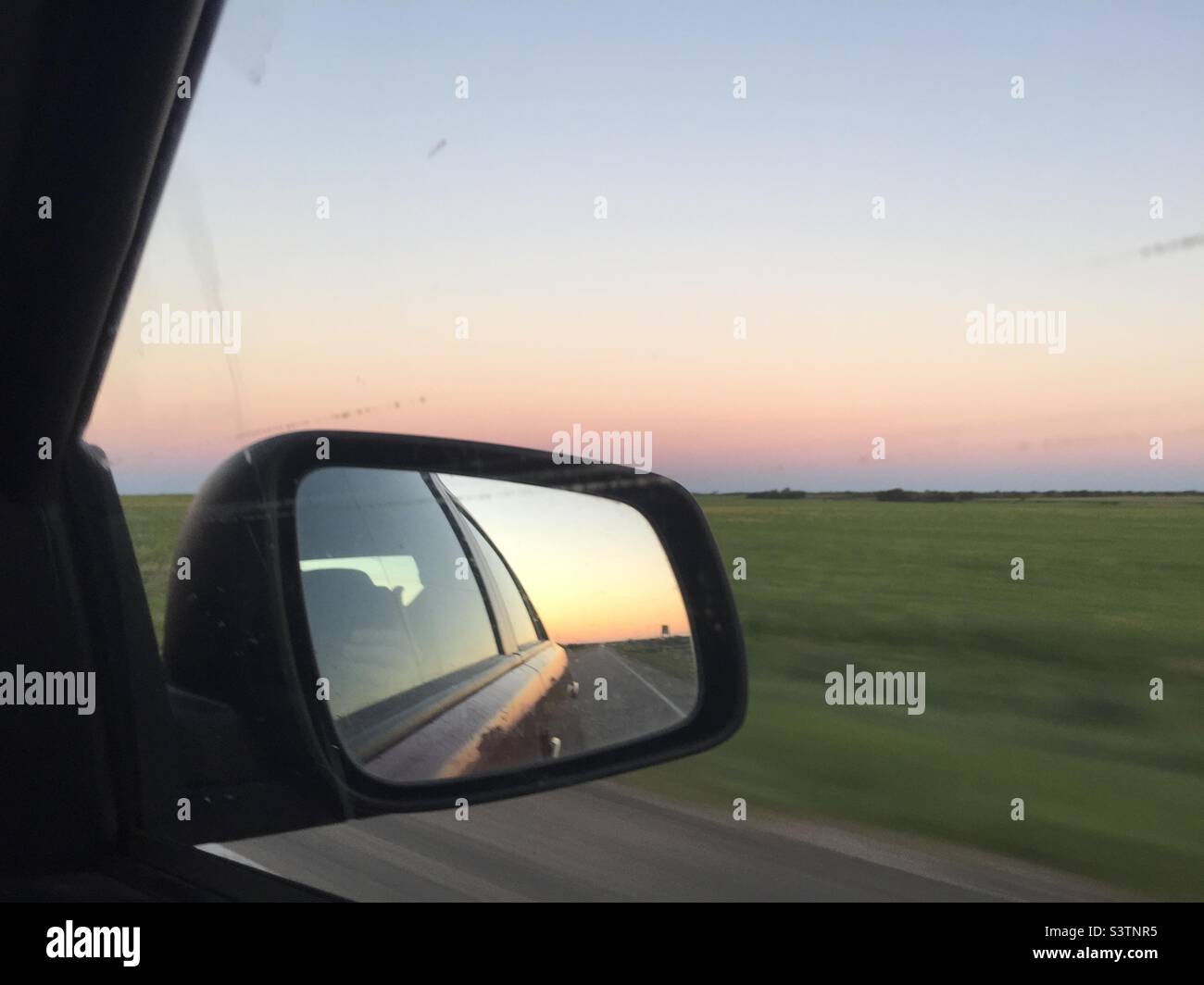 Der Sonnenuntergang wird durch das Autofenster und den Seitenspiegel gesehen - Smartphone-aufgenommenes Stockfoto