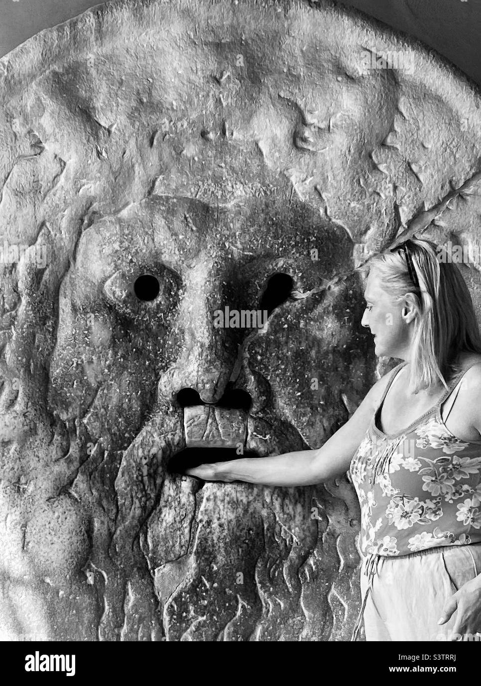 Schwarz-Weiß-Aufnahme einer Frau, die ihre Hand in den Mund der Wahrheit legt oder Bocca della veritas in Roma-Italien, die den klassischen Film Roman Holiday kopiert Stockfoto
