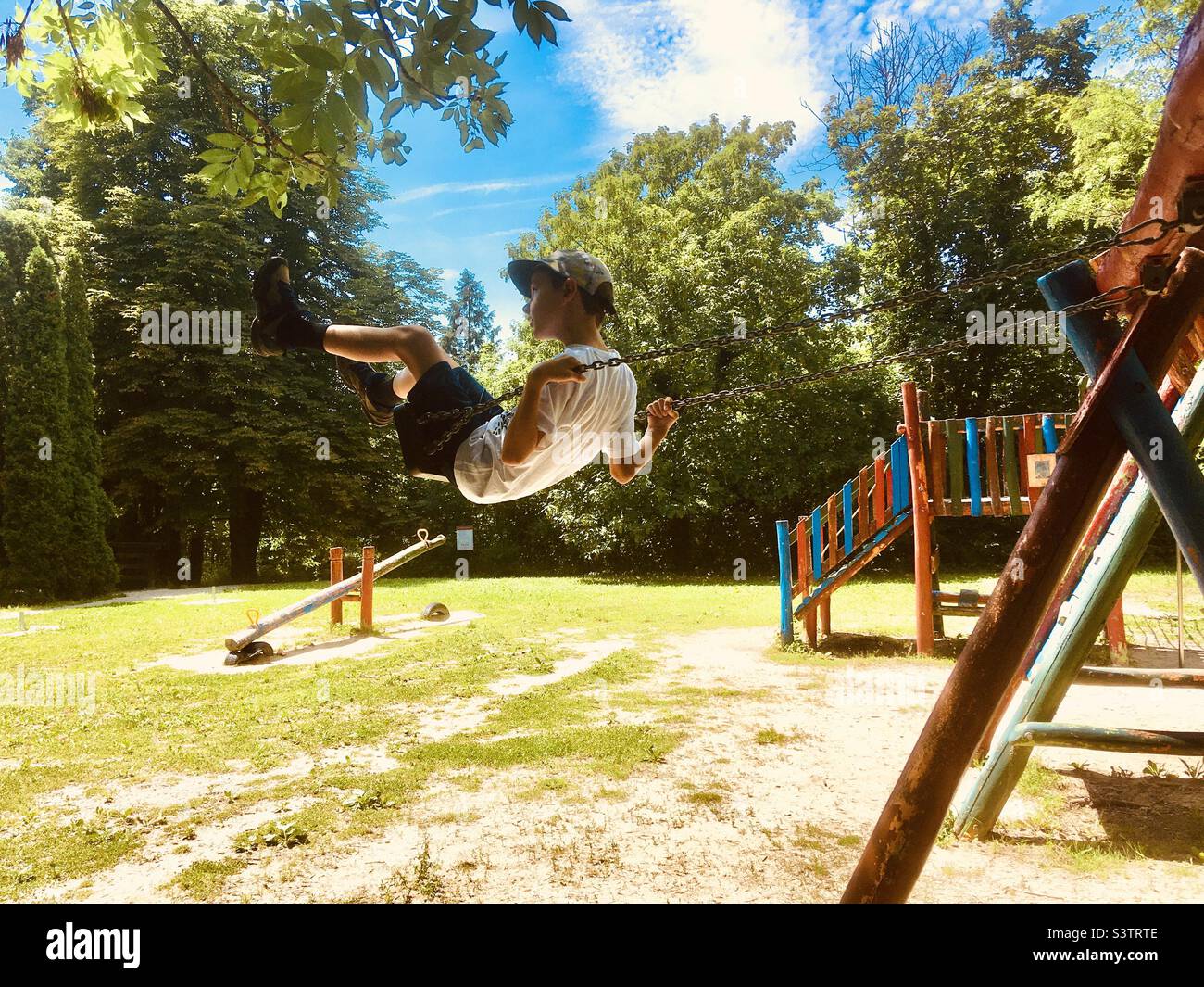 8 Jahre alter Junge Kind Kind schwingt auf dem Spielplatz so hoch, dass fast bis zu Ästen reichen Stockfoto