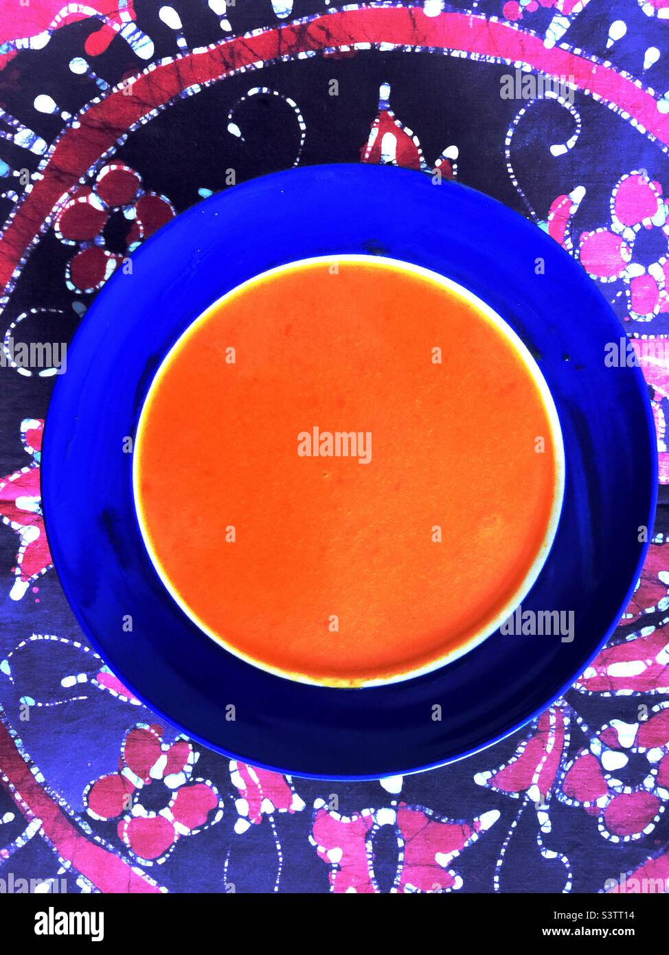 Leckere Tomatensuppe in einer weißen Schüssel mit blauem Rand. Batik Tischdecke. Stockfoto