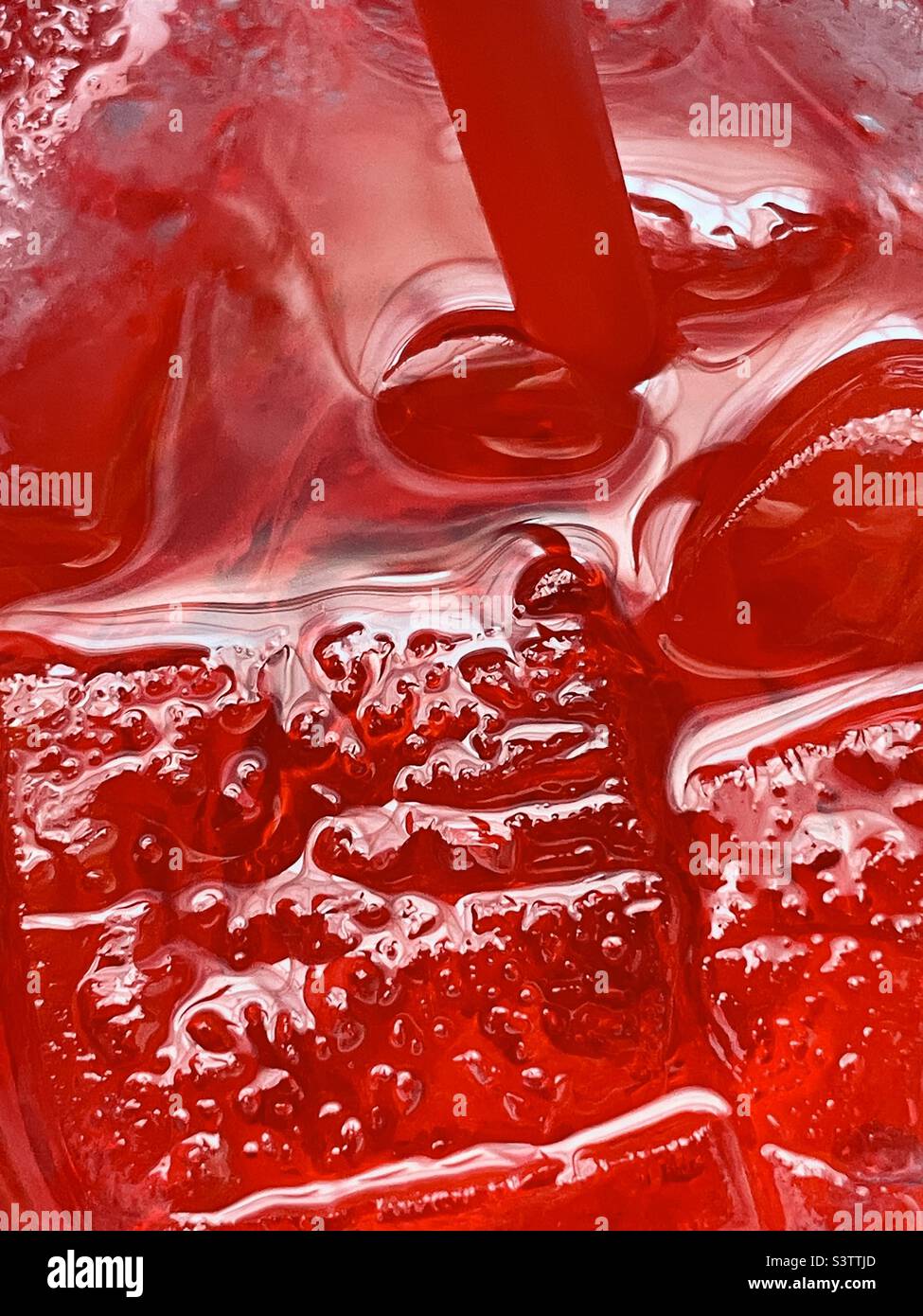 Blick hinunter in eine große Tasse eiskalten Kirschsprite. Die kalte rote kohlensäurehaltige Flüssigkeit, Stroh und Eis sorgen für eine tolle erfrischende Abstraktion. Stockfoto