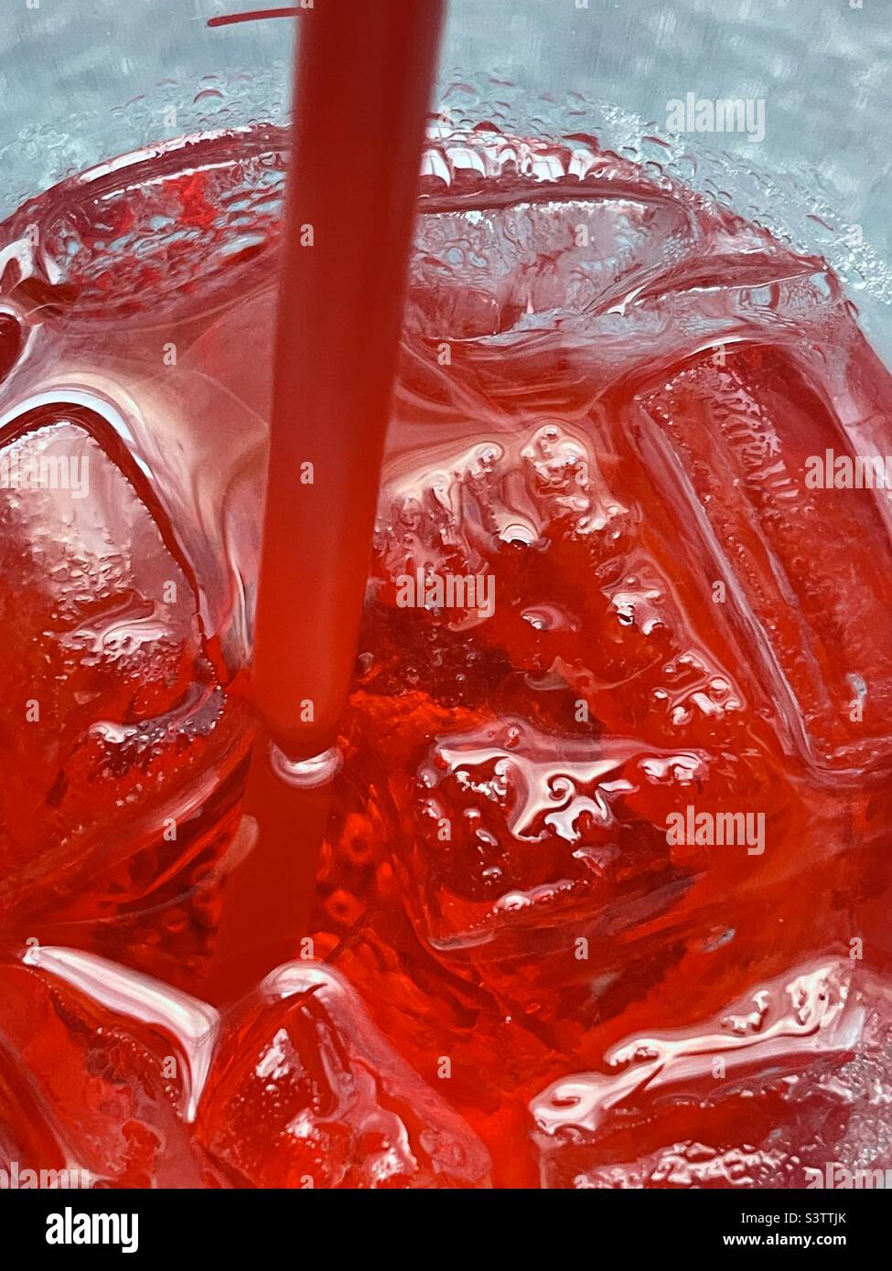 Blick hinunter in eine große Tasse eiskalten Kirschsprite. Die kalte rote kohlensäurehaltige Flüssigkeit, Stroh und Eis sorgen für eine tolle erfrischende Abstraktion. Stockfoto