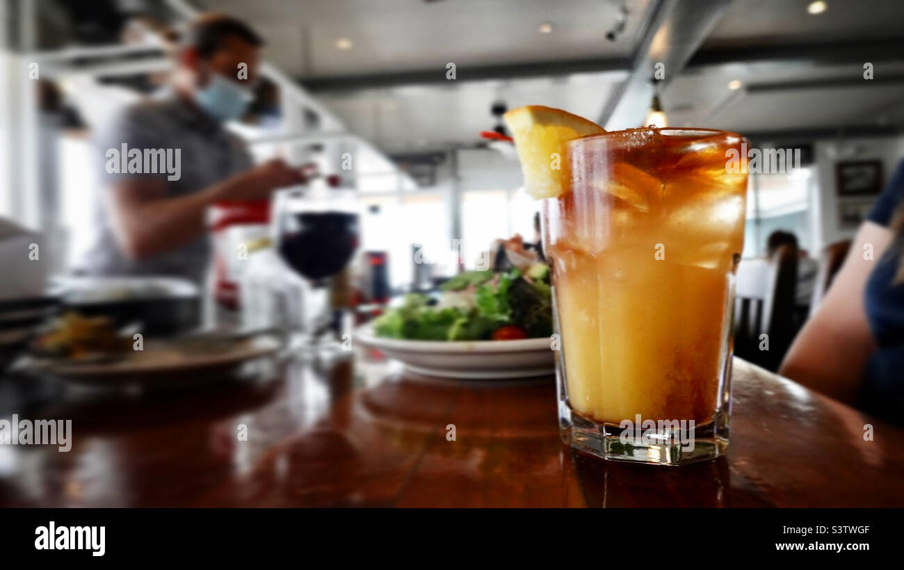 Mai Tai Cocktail mit orangefarbenem Segment, in einem kurzen Glas auf einer Theke, flacher Fokus, Salat im Hintergrund Stockfoto