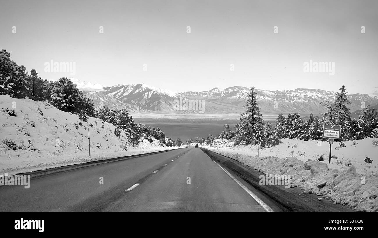 Blick auf verschneiten, nassen Highway, US Route 395, vorbei an Bergen, Mammoth Lakes, Kalifornien. Schwarz und Weiß Stockfoto