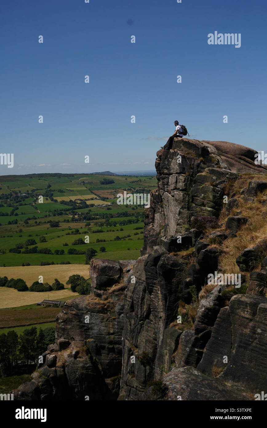 Mann, der am Rand einer Klippe sitzt und die Aussicht bewundert Stockfoto