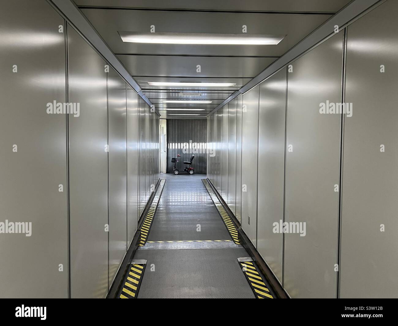 Elektrisch angetriebener Rollstuhl für Fluggäste mit Mobilitätsherausforderungen, der am Ende einer Düsenbrücke in einem Flughafen abgestellt wird - Smartphone-aufgenommenes Stockfoto