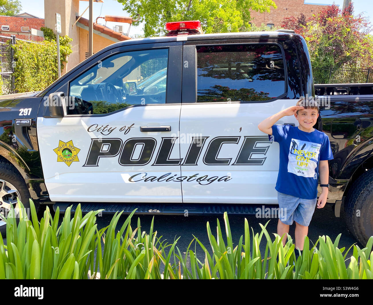 Ein Junge im Urlaub in Kalifornien posiert neben einem Polizeiauto in der Stadt Calistoga. - Smartphone-aufgenommenes Stockfoto