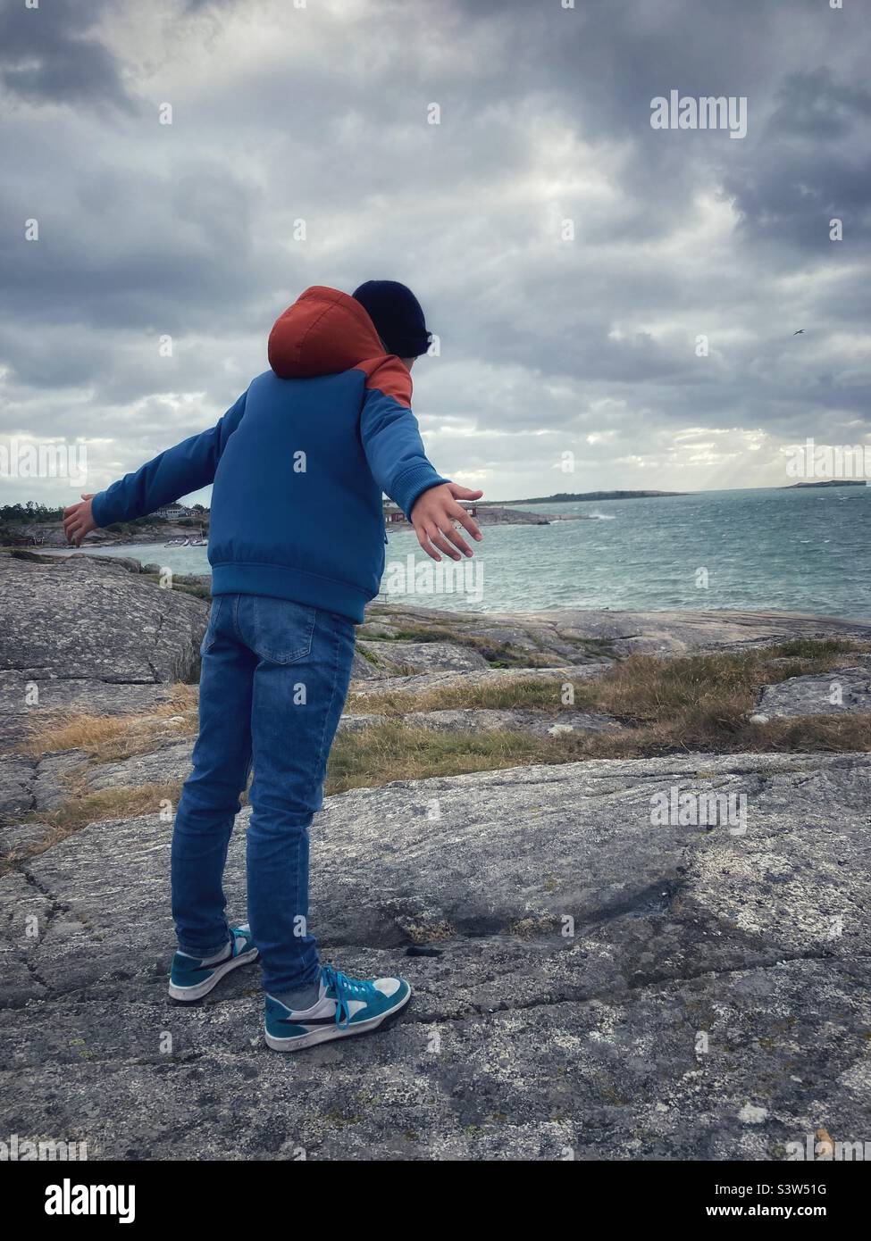 Ein vor-Teenager-Junge, der sich an der schwedischen Küste in einen starken Wind lehnt Stockfoto