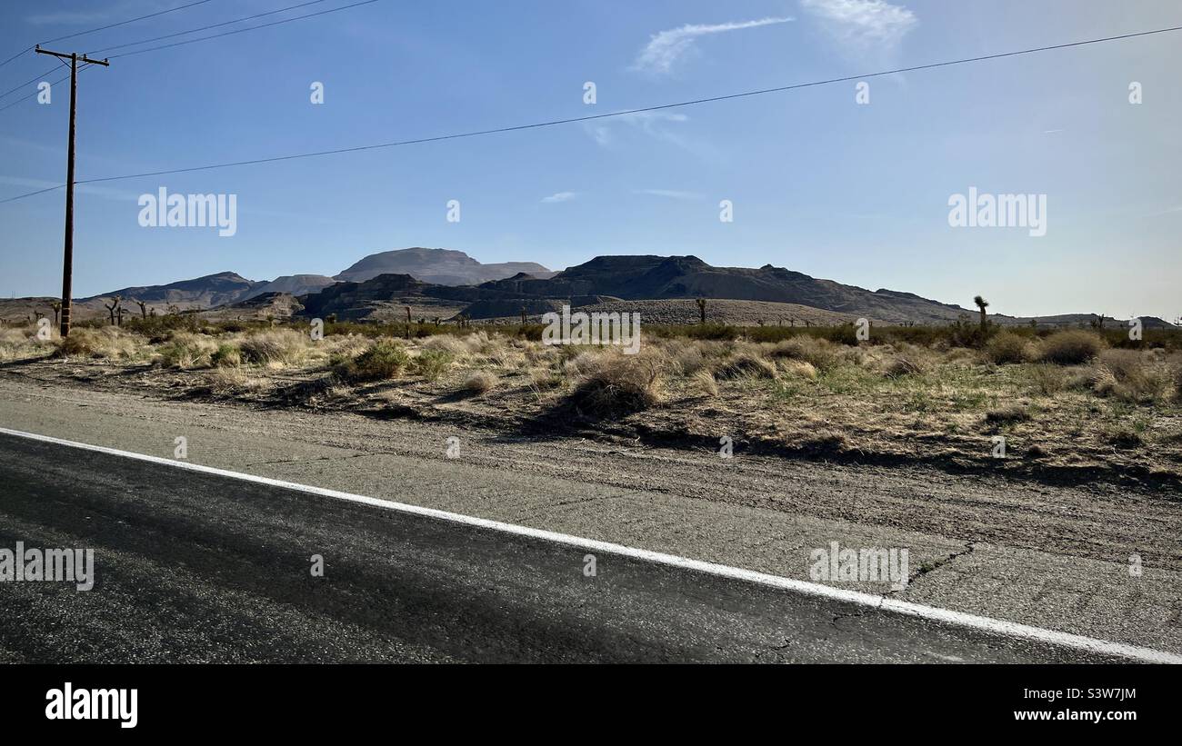 Blick vom Highway durch die Mojave-Wüste in Kalifornien, mit Buschland und Bergen in der Ferne, Telegrafenmasten und Drähten neben der Straße Stockfoto
