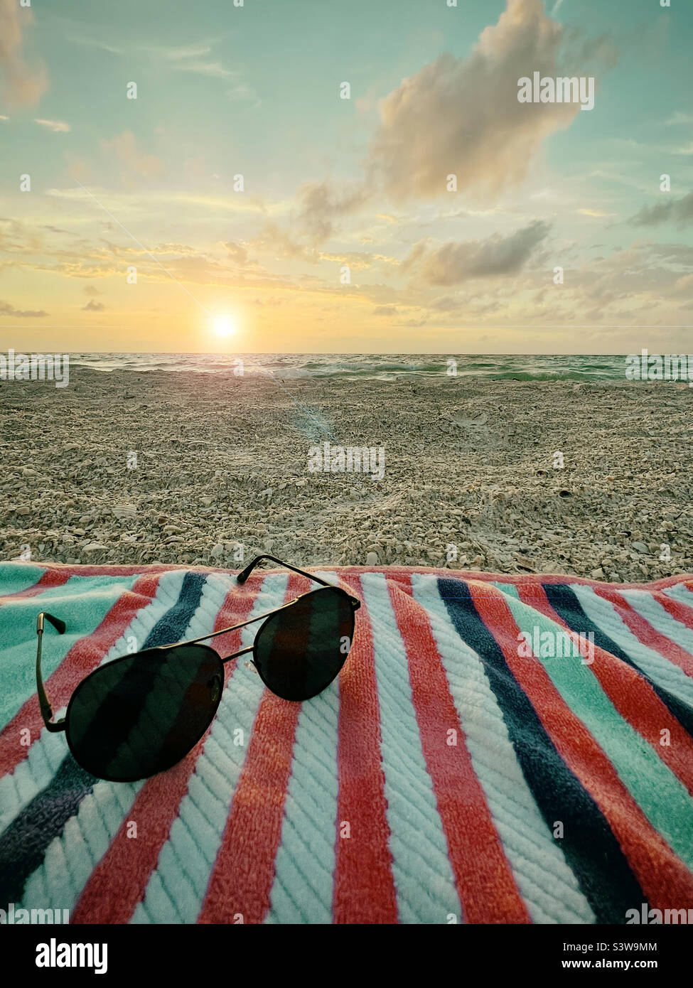 Sonnenglas auf Handtuch bei Sonnenuntergang am Strand Stockfoto