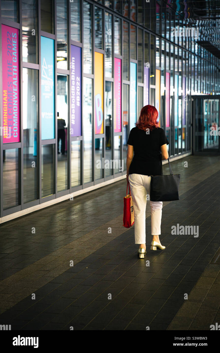 Rückansicht einer Dame mit roten Haaren, die während der Commonwealth Games 2022 in einer farbenfrohen Stadtumgebung von Birmingham unterwegs war Stockfoto