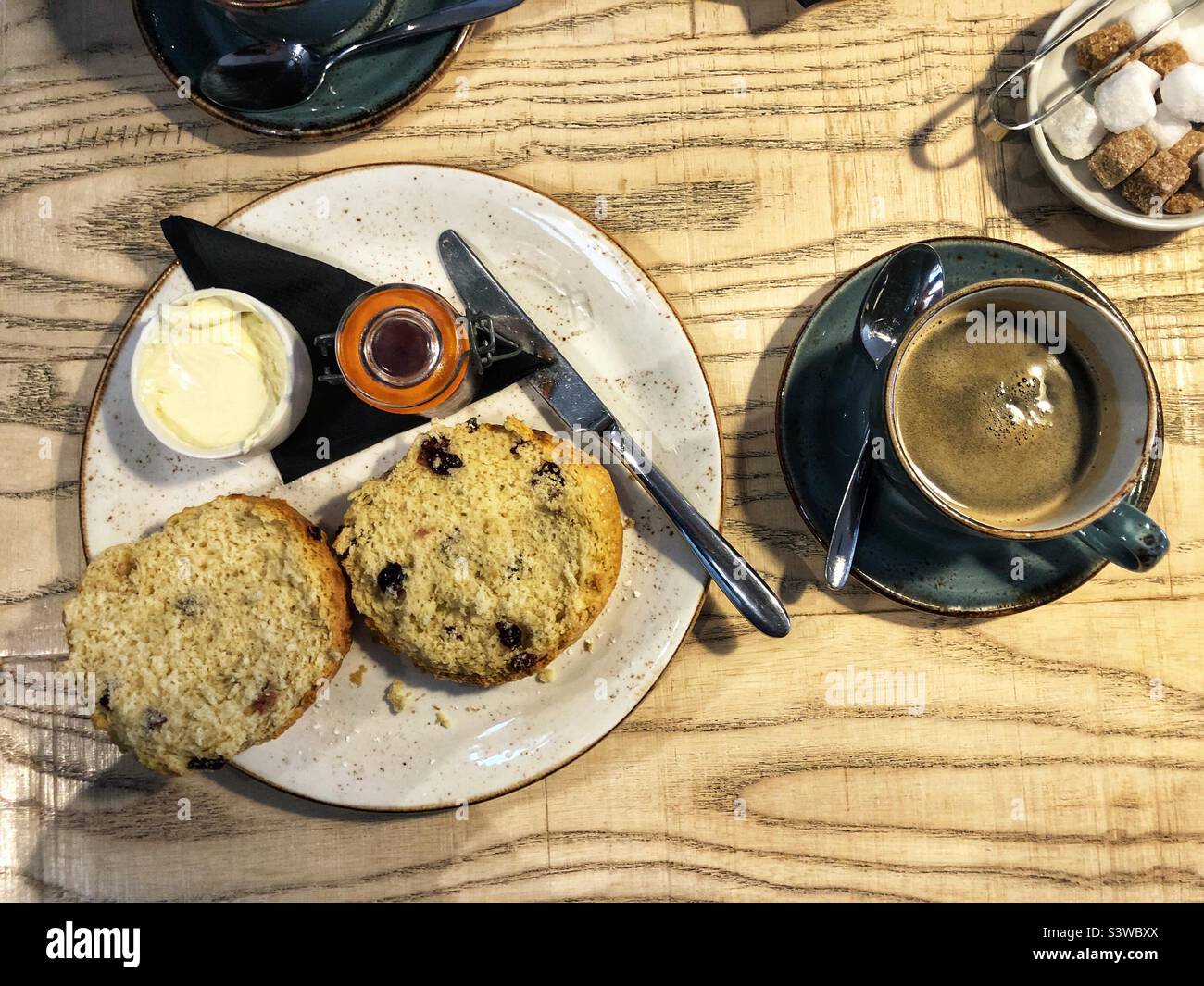 Schwarzer Kaffee und ein Fruchtscone mit Rahm und Marmelade - Smartphone-aufgenommenes Stockfoto