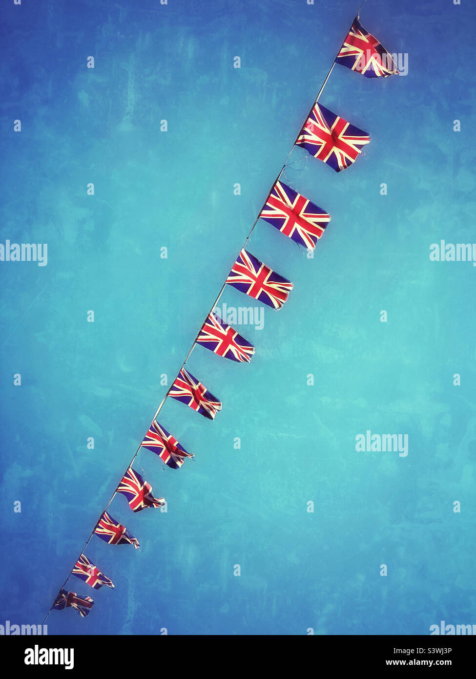Ein Grunge- und Retro-Effekt-Bild einer Linie von Union Jack-Flaggen. Der Bunten flattert im Wind eines britischen Sommertages und feiert das Platin-Jubiläum der Königin. Foto ©️ COLIN HOSKINS. - Smartphone-aufgenommenes Stockfoto