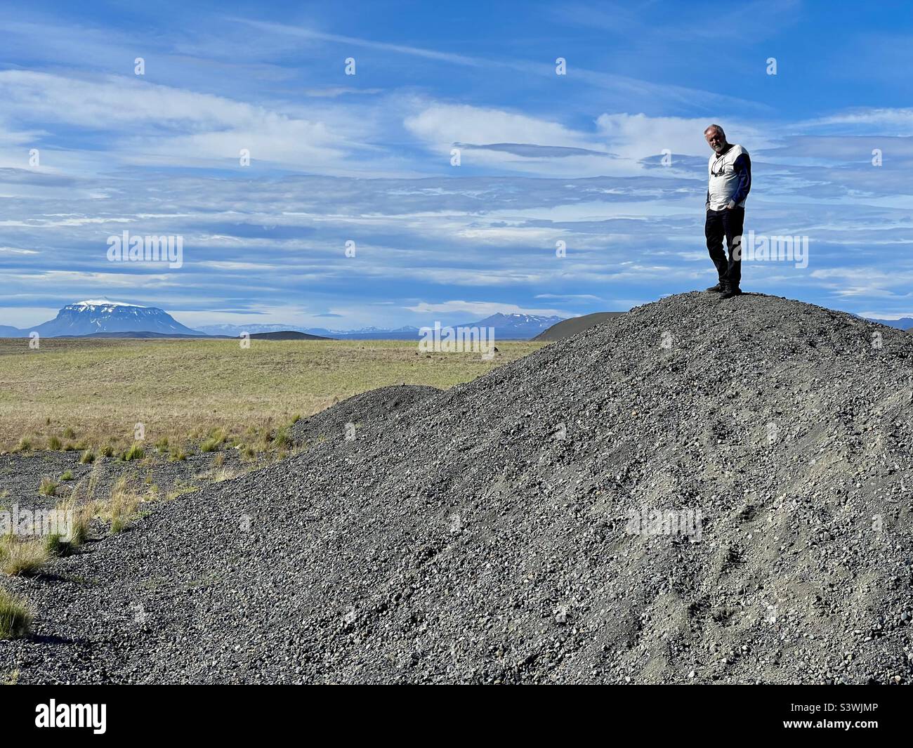 Einsamer Mann auf einem Schotterhügel mit Blick auf die Lavafelder und Berge im Osten Islands Stockfoto