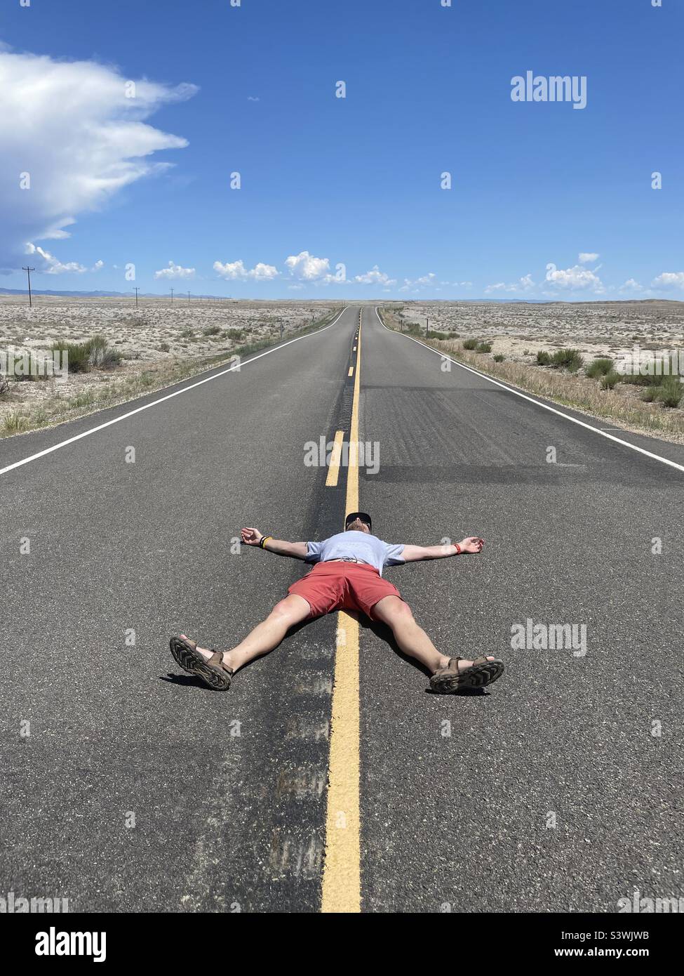 Ein Mann liegt mitten auf einer Straße, die Arme und Beine auseinander liegen - Smartphone-aufgenommenes Stockfoto