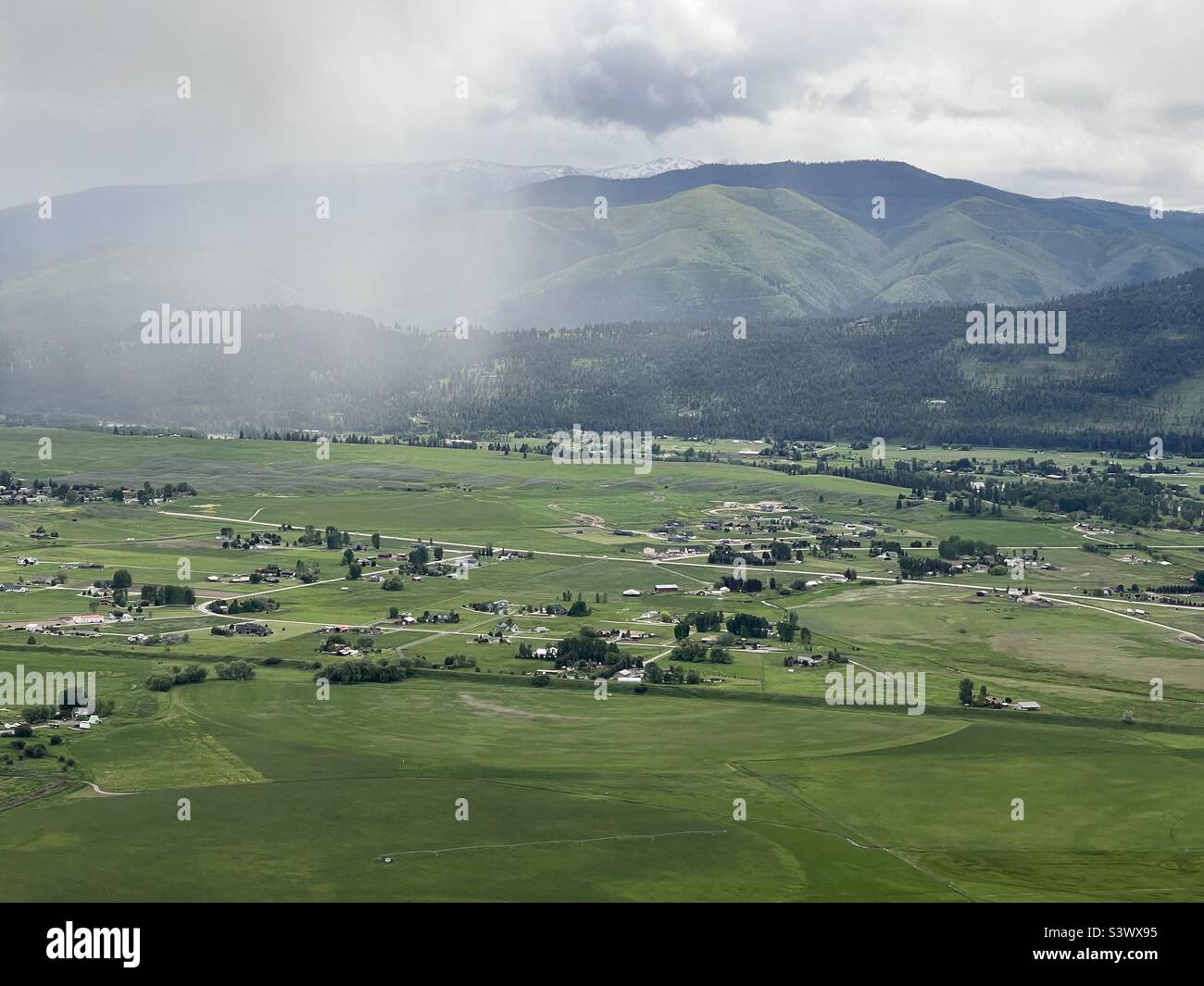 Luftaufnahme von üppigem, grünem Ackerland, Feldern, Häusern, Hügeln und Bergen in Missoula, Montana, USA. Regenwolken über dem Hotel Stockfoto