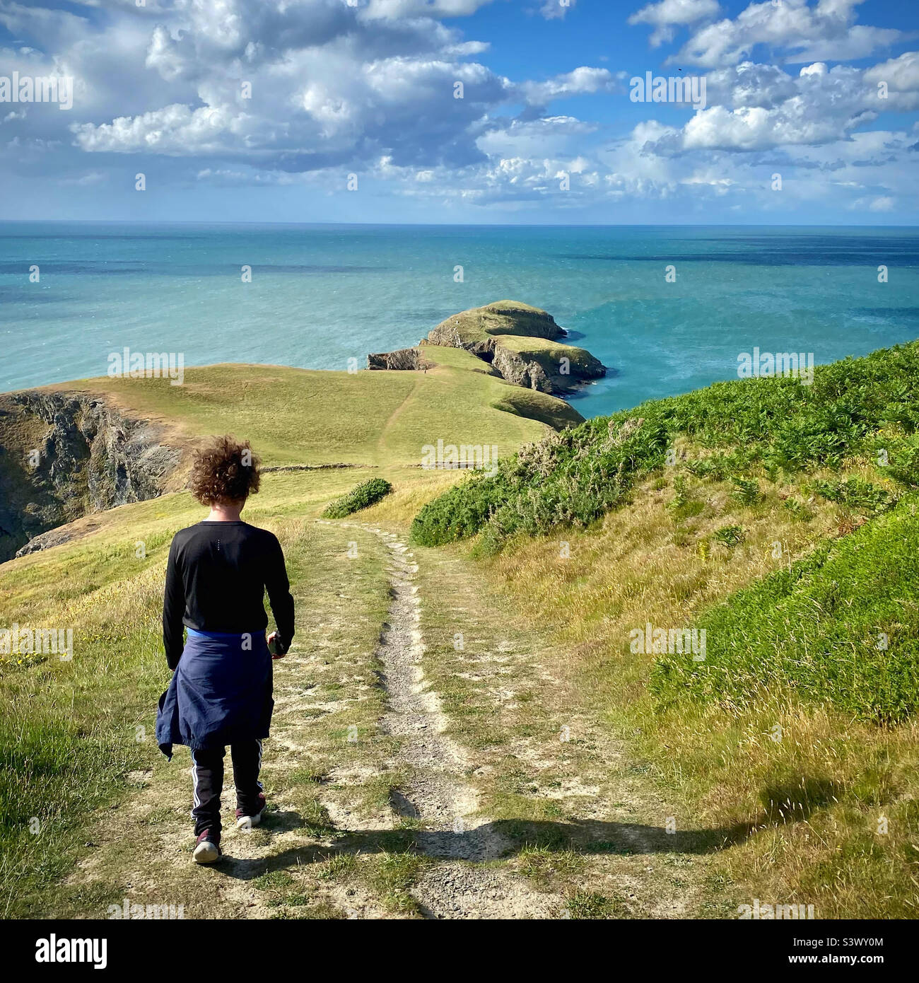 Teenager, der auf dem Küstenpfad von Ceredigion in Wales, Großbritannien, in der Nähe von Llangrannog läuft Stockfoto