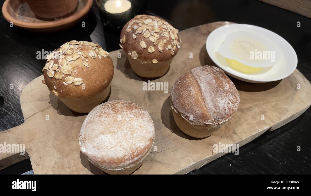 Kleine Brötchen auf Holzpaddel mit Hafer und Mehl bestäubt und mit einem kleinen Untertasse mit Butter serviert - Smartphone-aufgenommenes Stockfoto