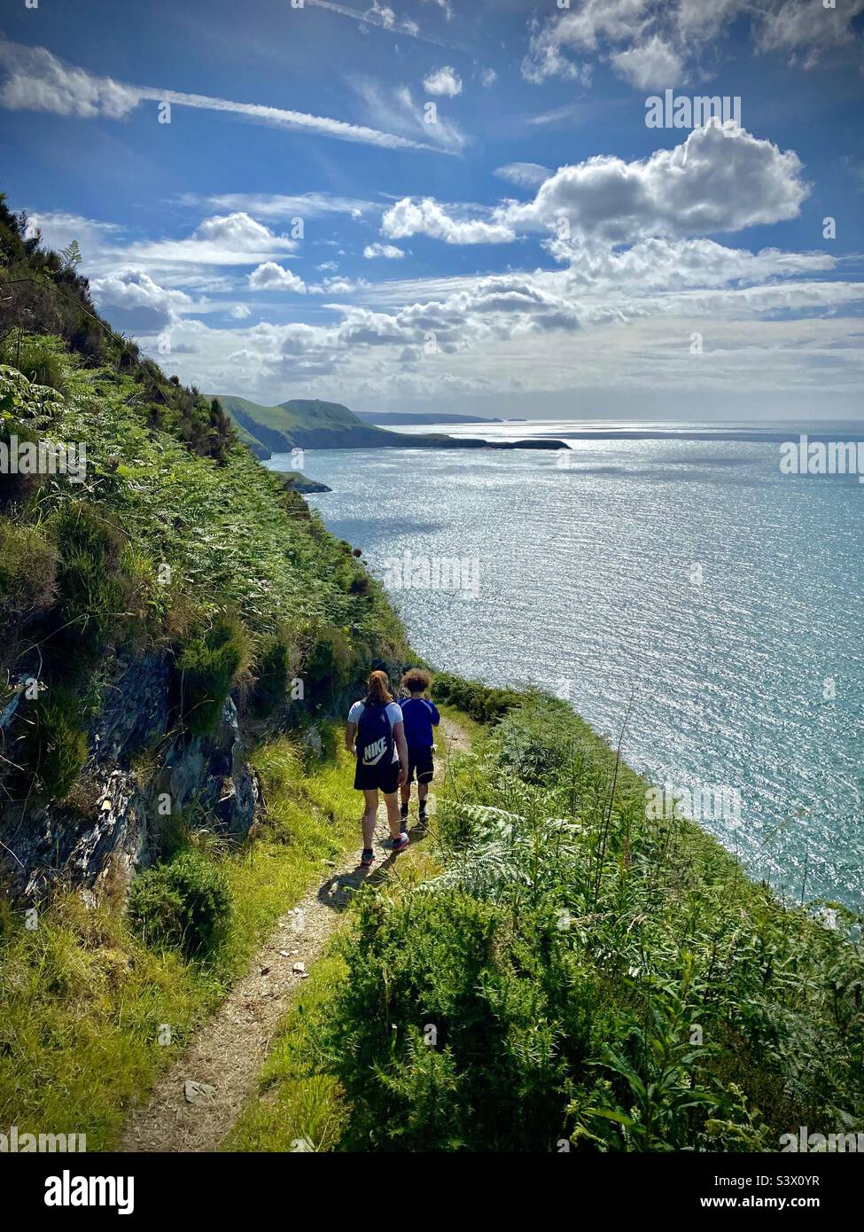 Eine Familie, die einen dramatischen Abschnitt des Ceredigion Coast Path in der Nähe von Llangrannog in West Wales entlang geht Stockfoto