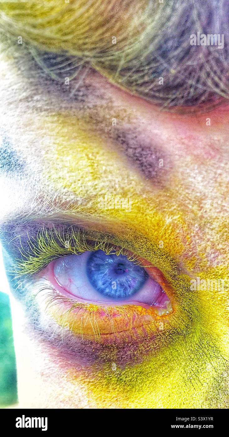 Hellblaues Auge auf dem Gesicht mit Pulverfarbe bedeckt, hauptsächlich gelbe Nahaufnahme Stockfoto