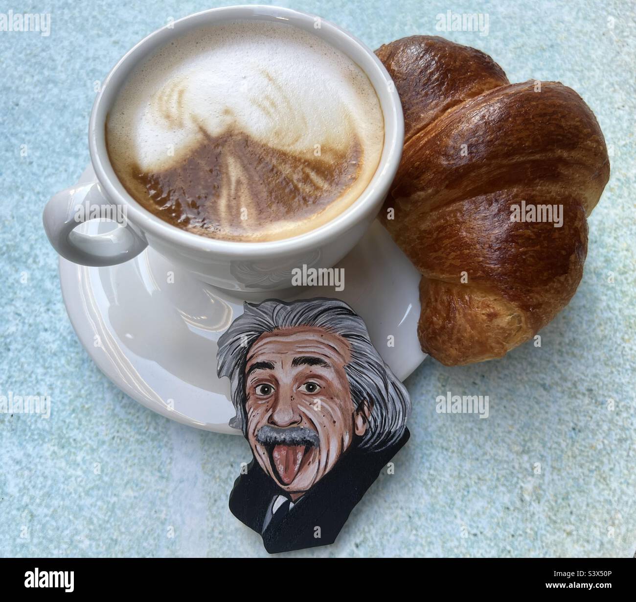 Cleveres Frühstück an der Bar mit Croissant, Cappuccino und einem kunstvoll von Einstein gemalten Gesicht Stockfoto