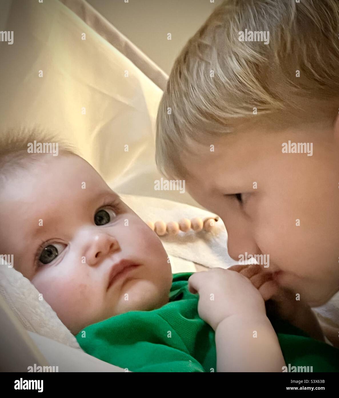 Ein Kleinkind bewundert sanft seine kleine 6 Monate alte Schwester. Stockfoto