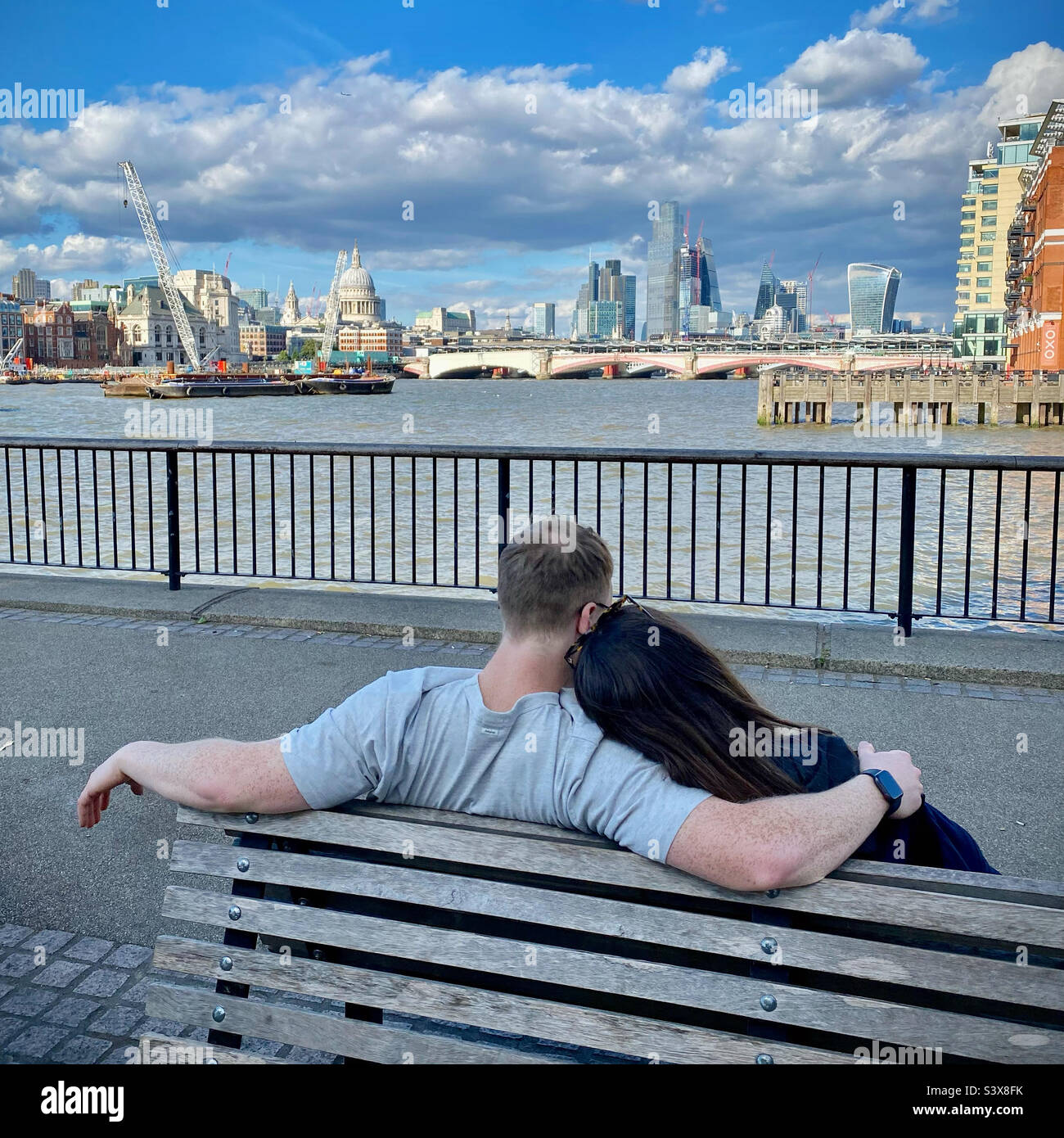 Ein Paar, das auf einer Bank am Londoner Südufer sitzt und romantisch entlang der Themse in Richtung City of London blickt Stockfoto
