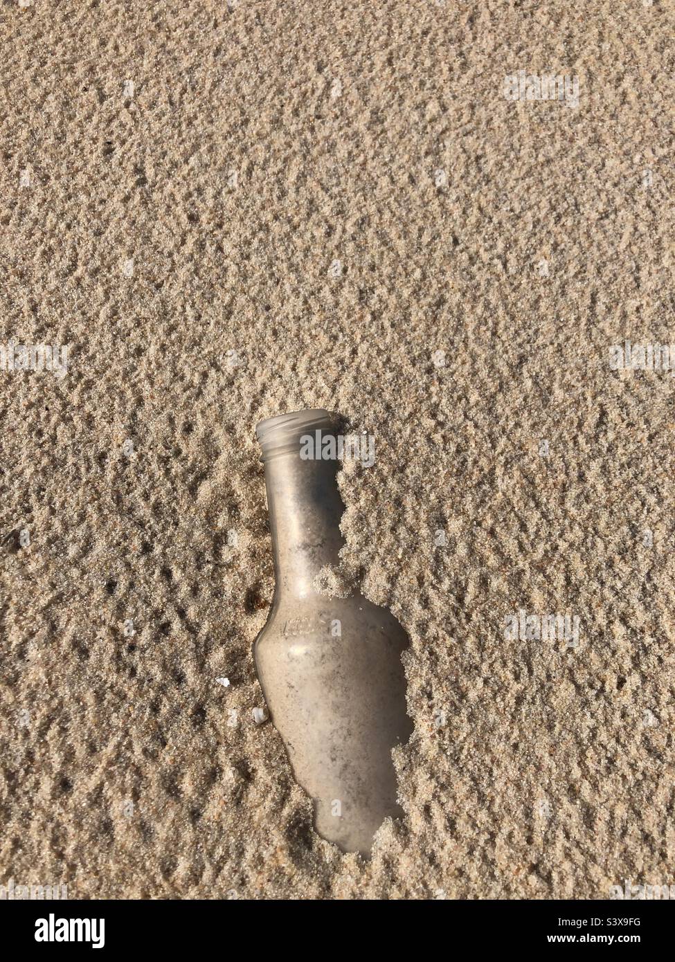 Eine Flasche, die halb im Sand vergraben ist. Stockfoto