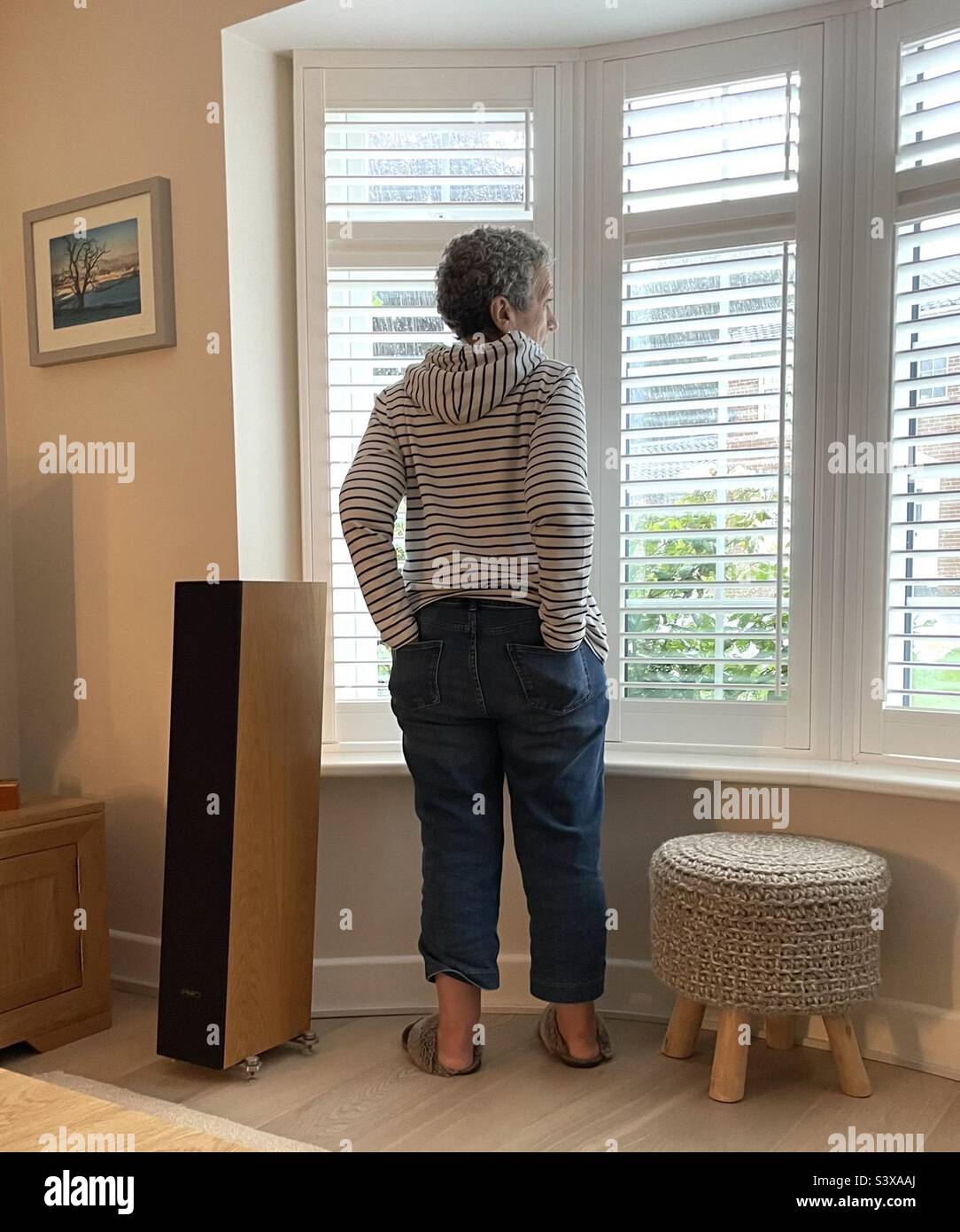 Die Dame entspannte sich und schaute erwartungsvoll aus dem Fenster zu Hause mit den Händen in der Gesäßtasche Stockfoto