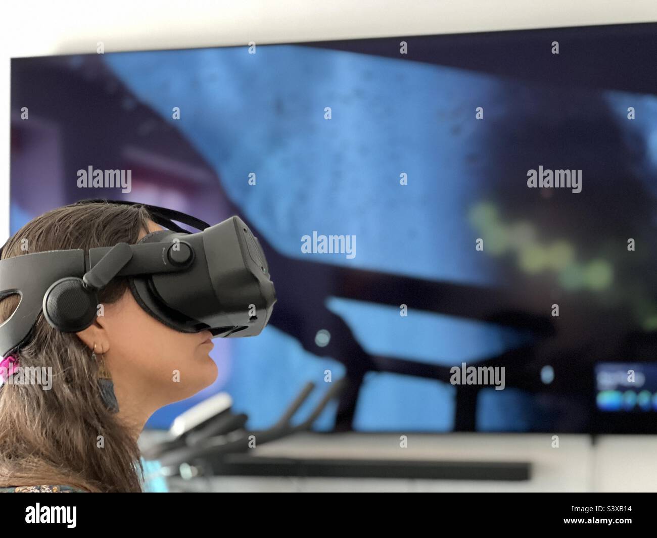 Mädchen mit VR-Headset und unscharfem Spiel auf dem Bildschirm im Hintergrund. - Smartphone-aufgenommenes Stockfoto