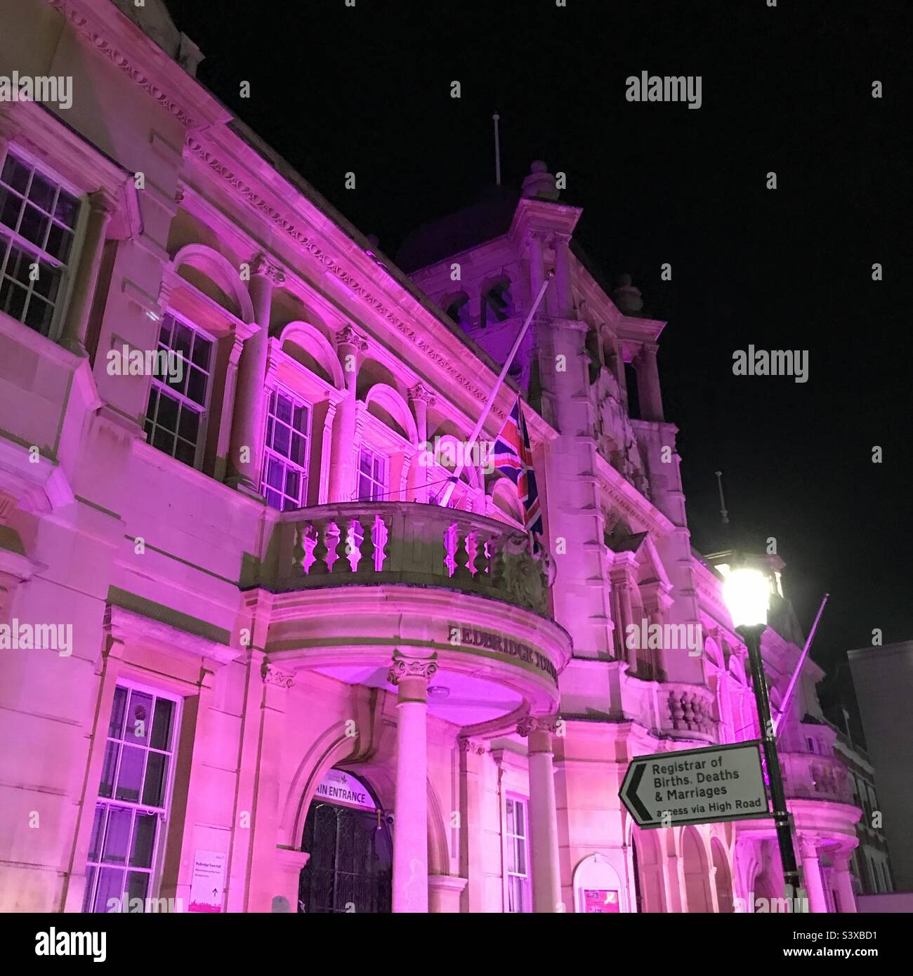 Flagge am halben Mast vor dem Rathaus von Redbridge am Vorabend der Beerdigung der Königin. Rathaus in lila zum Gedenken an Königin Elizabeth beleuchtet. Stockfoto